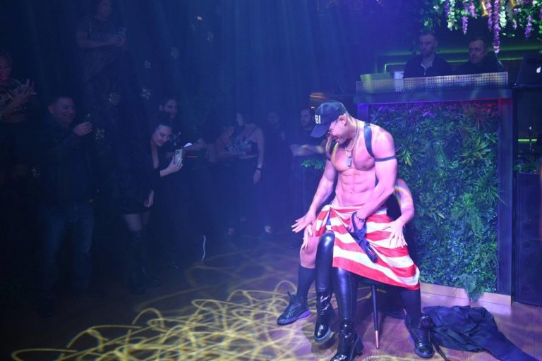 Male stripper performing at a lively bachelorette party in NYC with excited guests cheering