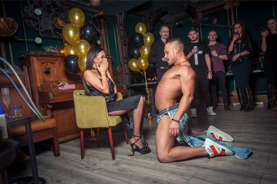 A male stripper performing at a vibrant bachelorette party in NYC, surrounded by a cheering group of friends.